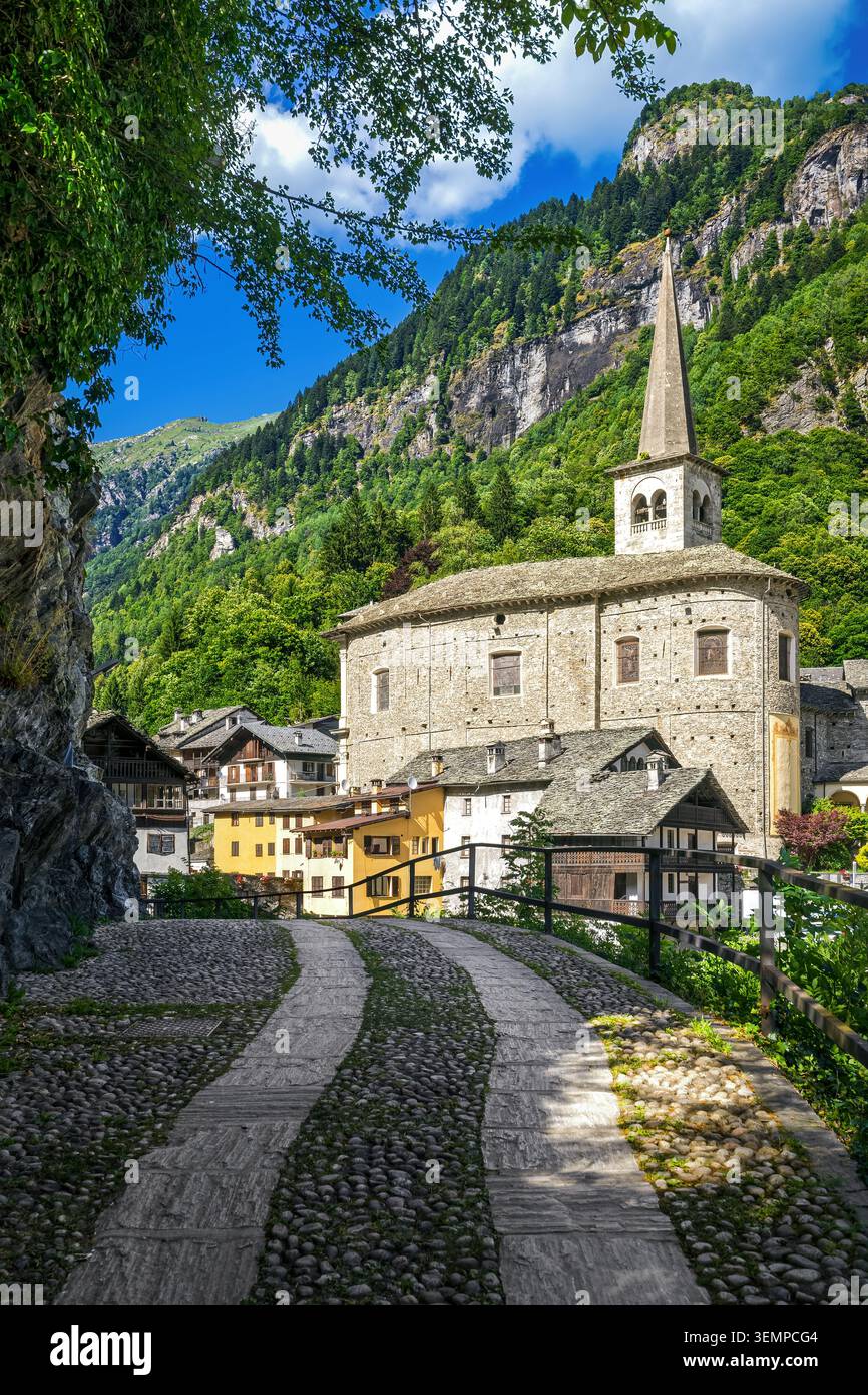 Une vue panoramique sur l'église historique en pierre et les maisons alpines traditionnelles le long d'un chemin pavé dans les montagnes verdoyantes de Campertogno, en Italie Banque D'Images