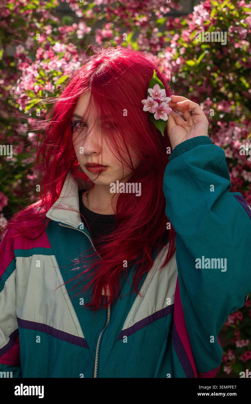 Jeune femme mettant une fleur rose dans les cheveux roux Banque D'Images