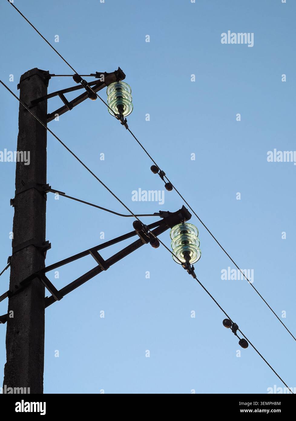 Ligne d'alimentation haute tension avec isolateurs en verre. Vue en angle bas des isolateurs de suspension en verre et des fils électriques sur un poteau utilitaire en béton, ciel dégagé. Banque D'Images