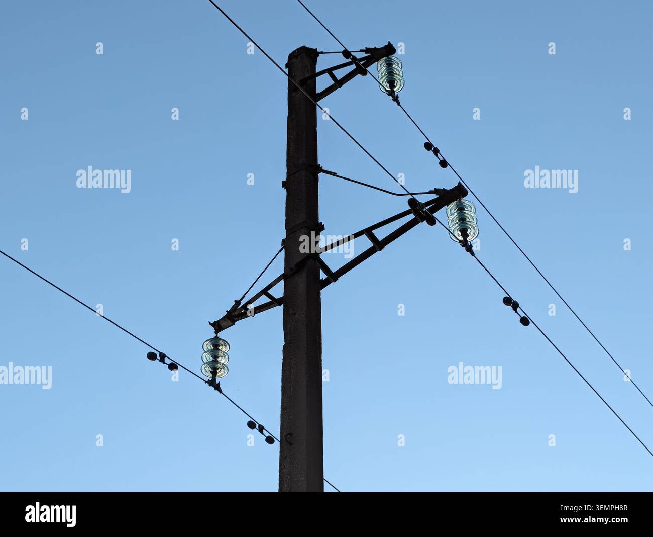 Silhouette de ligne de puissance haute tension. Prise de vue à faible angle d'isolateurs de suspension en verre et de câbles électriques sur un grand poteau en béton contre le ciel bleu Banque D'Images