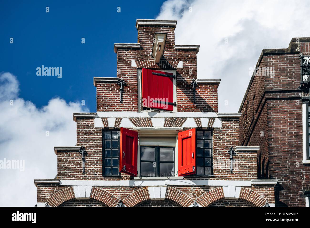 Façade traditionnelle néerlandaise à pignon en escalier avec volets rouges distinctifs contre un ciel bleu dans le centre historique d'Amsterdam, pays-Bas Banque D'Images