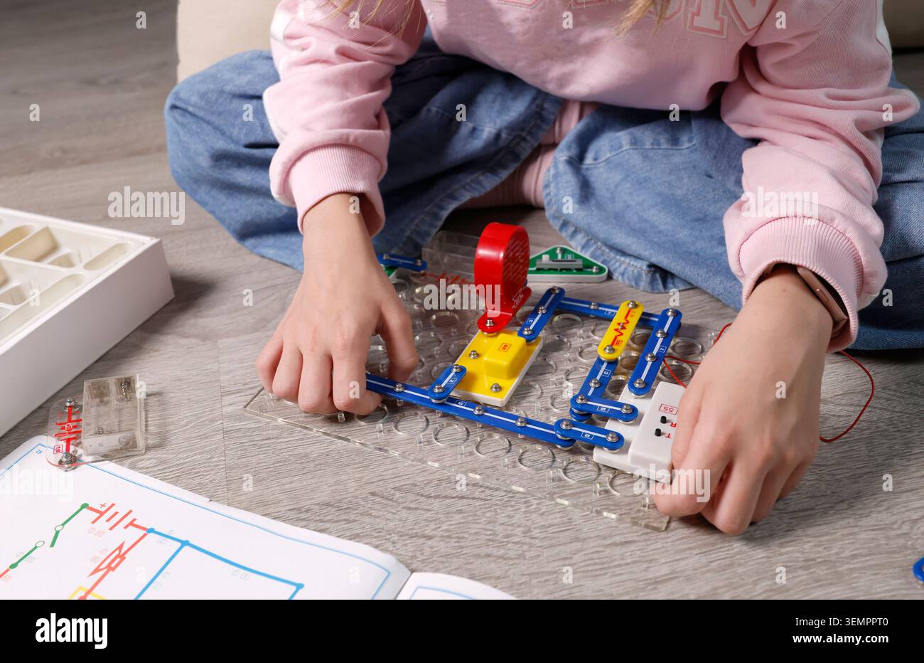 Main d'enfant gros plan assemblage des blocs de configuration du circuit électronique sur la plaque de base transparente. Activité pédagogique de laboratoire STEM pour les sciences physiques Banque D'Images