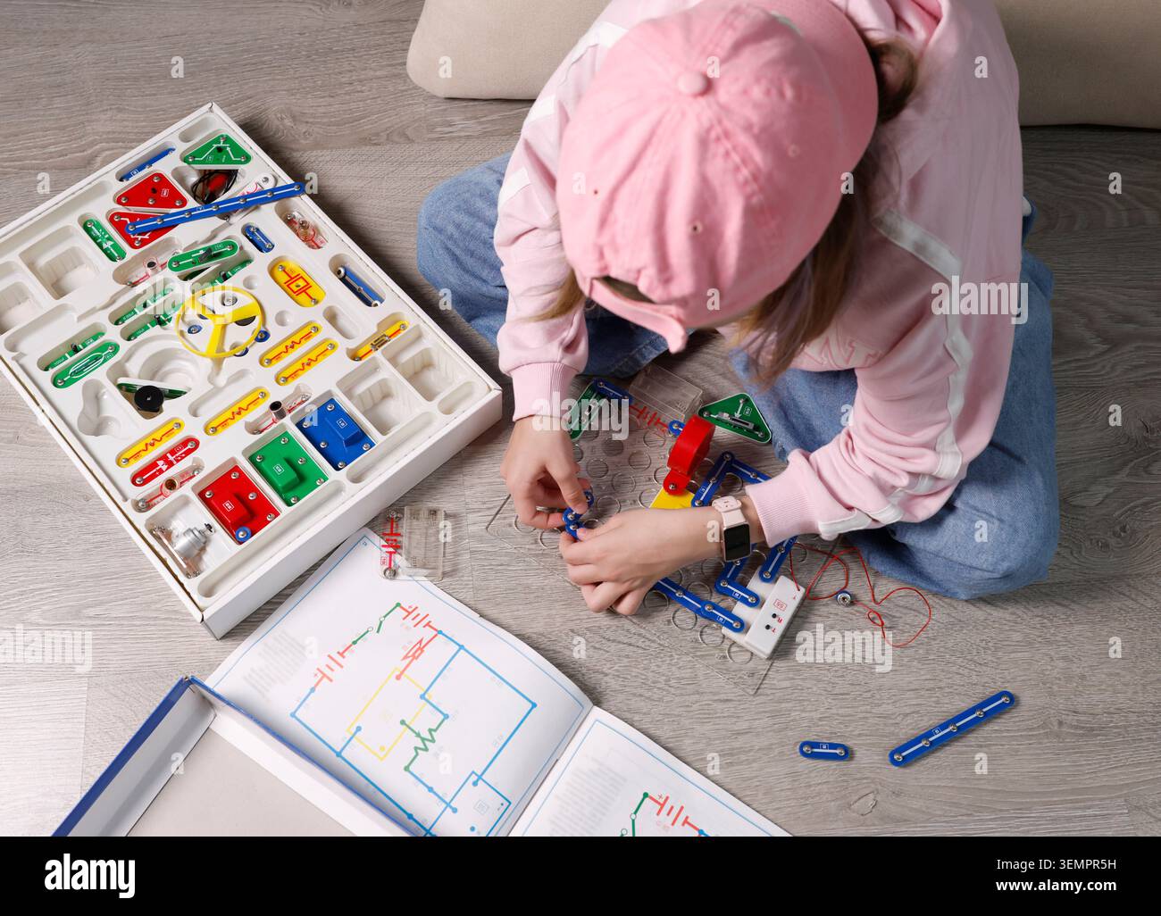 Enfant portant un capuchon rose et une montre intelligente assemblant des blocs de circuit électronique sur la plaque de base de la grille. Activité pédagogique de laboratoire STEM pour la physique Banque D'Images