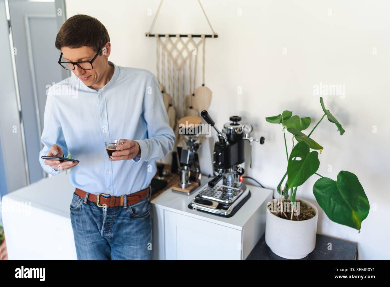 Homme prenant une pause avec expresso et smartphone, cafetière manuelle en arrière-plan Banque D'Images