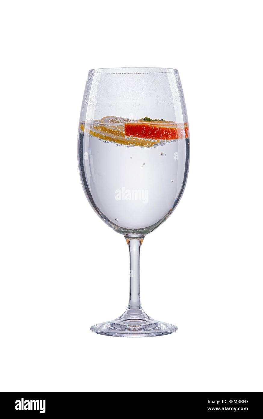 Un verre à vin rempli d'eau pétillante claire, de bulles et de tranches d'agrumes flottantes se dresse sur un fond blanc. Banque D'Images