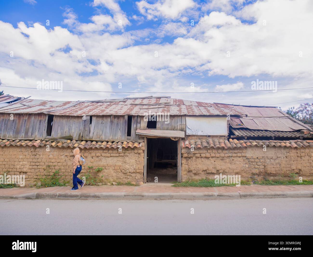 Une femme passant devant la façade grincée d'une menuiserie sombre, avec un vieux mur d'adobe, dans la ville de Villa de Leyva dans les Andes orientales Banque D'Images