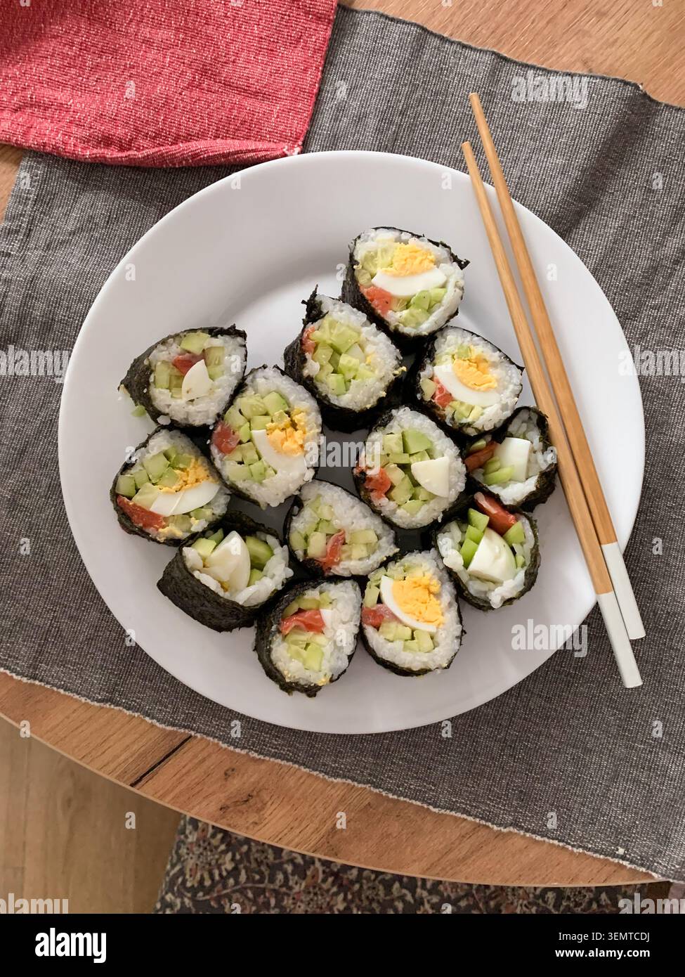Les rouleaux de sushi sont disposés soigneusement sur une assiette blanche. Les rouleaux contiennent du concombre, du poisson rouge et des œufs. Ils sont servis avec des baguettes sur un m bleu et vert Banque D'Images