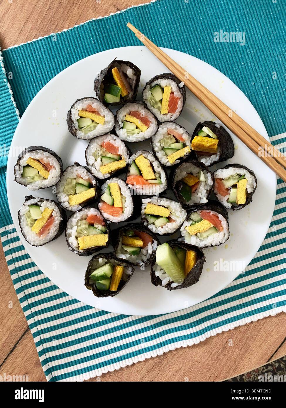 Les rouleaux de sushi sont disposés soigneusement sur une assiette blanche. Les rouleaux contiennent du concombre, du poisson rouge et des œufs. Ils sont servis avec des baguettes sur un m bleu et vert Banque D'Images