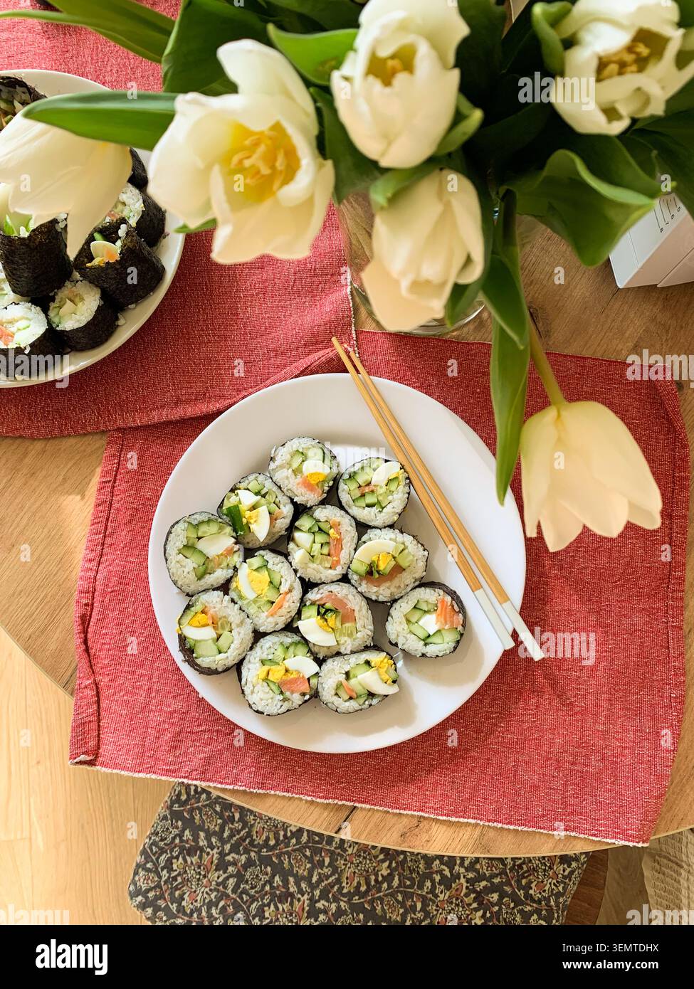 Les rouleaux de sushi sont disposés soigneusement sur une assiette blanche. Les rouleaux contiennent du concombre, du poisson rouge et des œufs. Ils sont servis avec des baguettes sur un tapis bleu et vert Banque D'Images