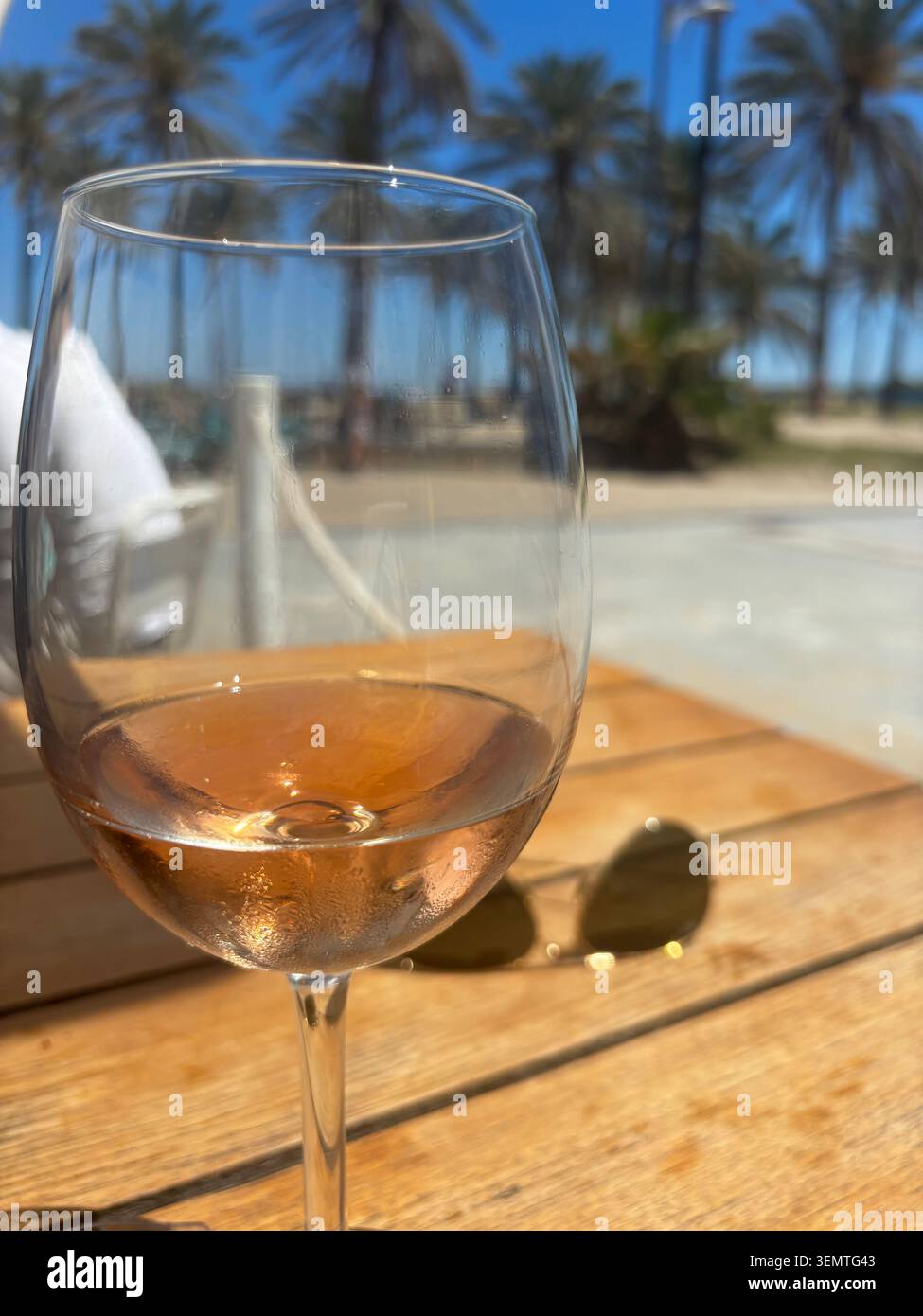 Un verre de vin rosé sur une table de café près de la plage de Malvarrosa à Valence, en Espagne, avec des palmiers et le front de mer méditerranéen en arrière-plan. - Image de stock capturée avec un smartphone