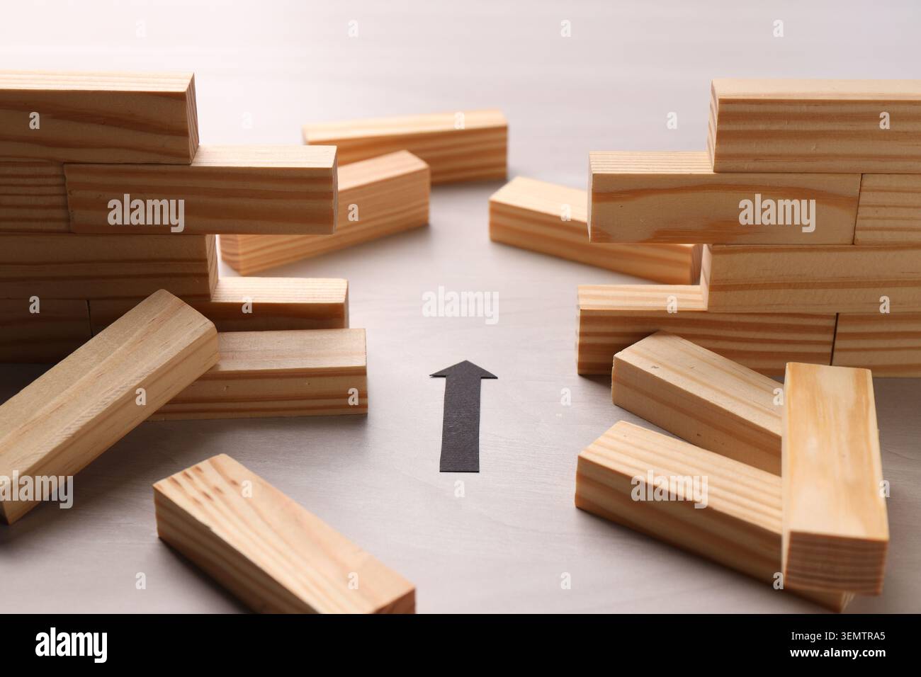 Mur en bois effondré fait de blocs et flèche de papier sur la table, gros plan. Surmonter les obstacles Banque D'Images