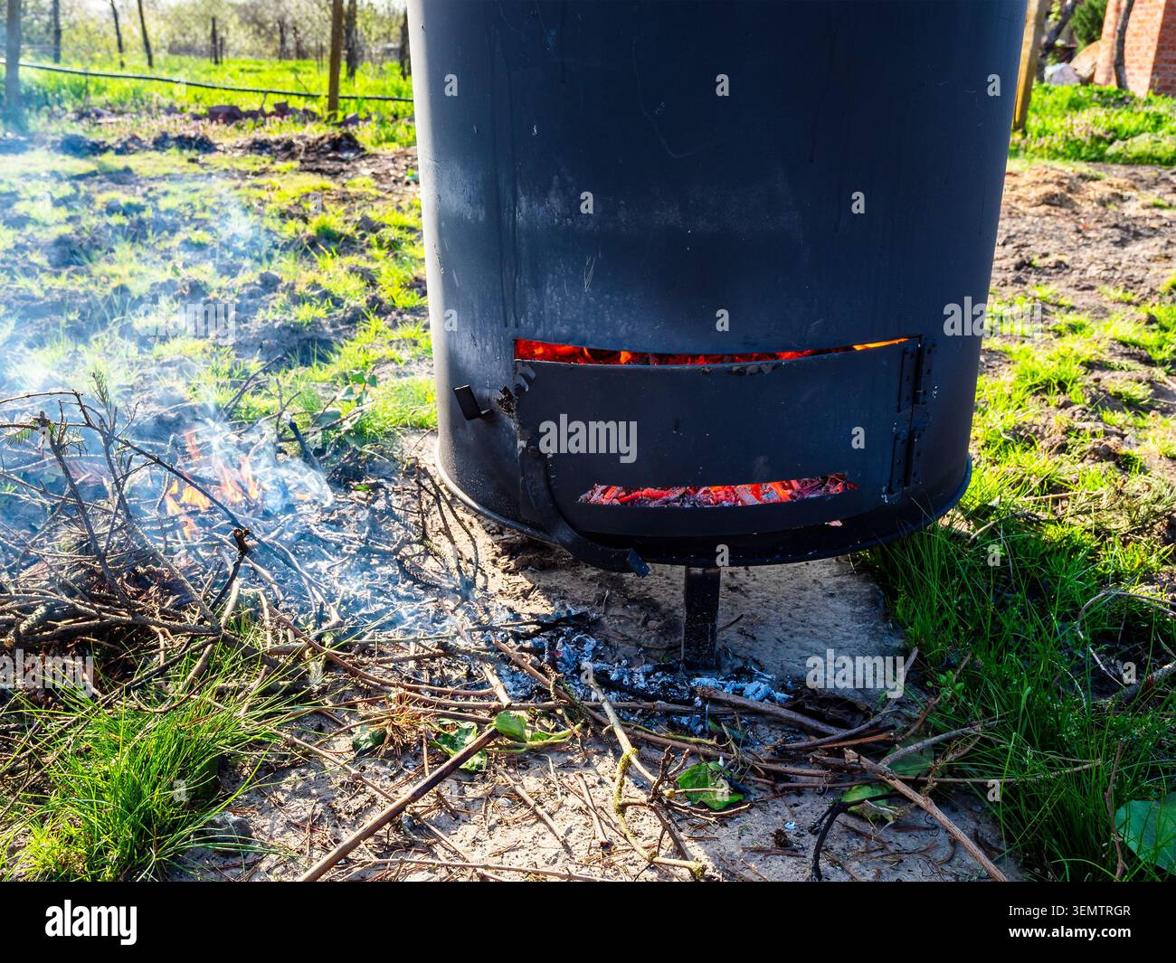 les charbons sont en train de fondre derrière l'amortisseur du poêle avec la fosse à cendres fermée dans le baril pour brûler les ordures dans le jardin du village le jour ensoleillé du printemps Banque D'Images