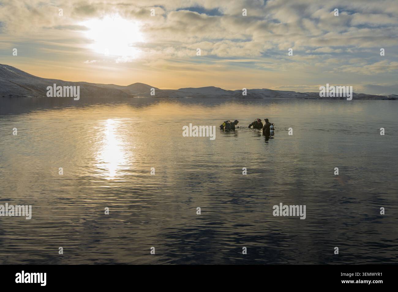 Plongeurs se préparant à plonger dans le lac Kleifarvatn sur la péninsule de Reykjanes, en Islande, avec un soleil hivernal bas et une eau calme. Banque D'Images