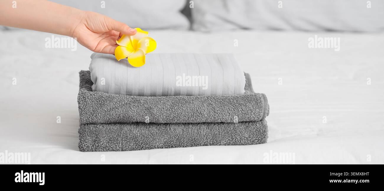 Main plaçant la fleur de plumeria jaune sur la pile de serviettes grises fraîchement pliées et le linge blanc sur le lit Banque D'Images
