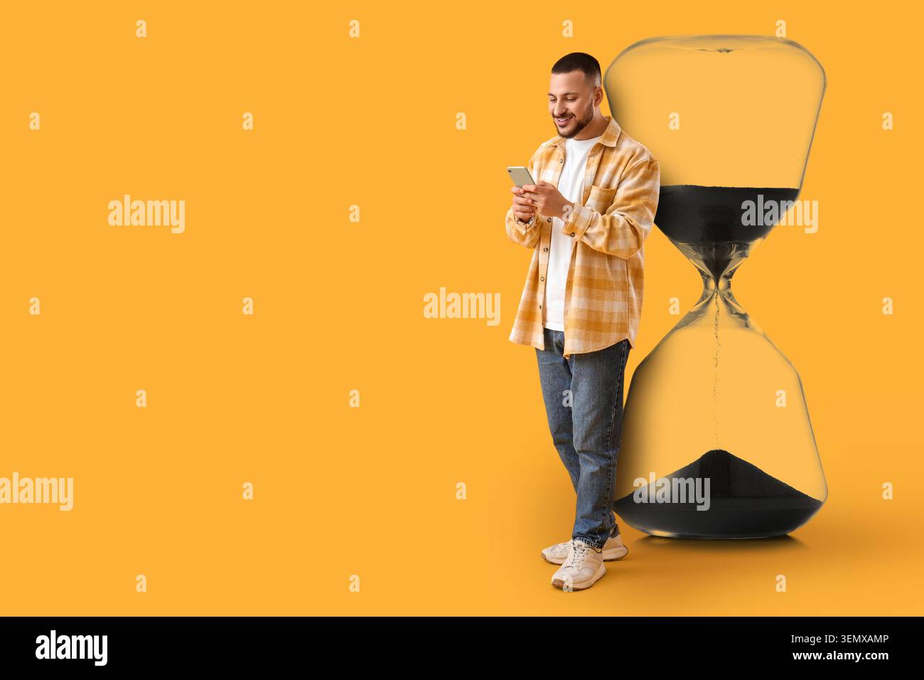 Jeune homme utilisant un smartphone à côté d'un grand sablier, la gestion du temps et le concept d'utilisation des appareils numériques, un jeune homme est activement engagé avec son smartph Banque D'Images