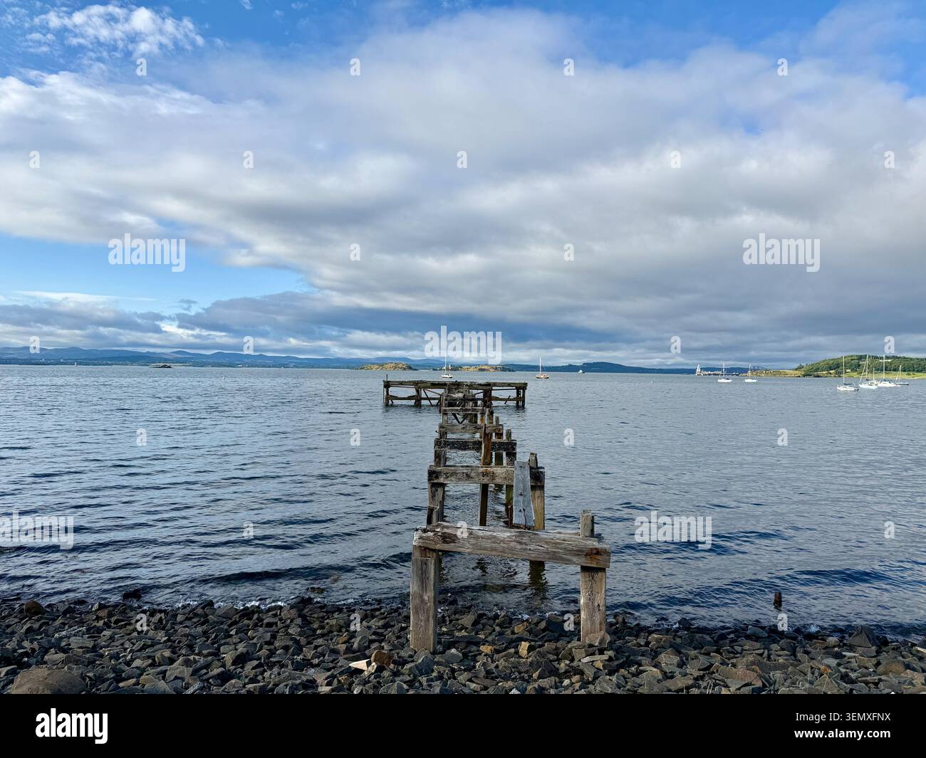 Une jetée en bois en ruine sur un loch de mer écossais calme, avec des voiliers amarrés en arrière-plan - Image de stock capturée avec un smartphone