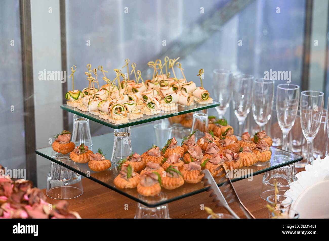 Table de buffet gastronomique avec profiteroles farcies de pâtisserie et canapés au concombre sur des stands en verre à plusieurs niveaux vue rapprochée Banque D'Images