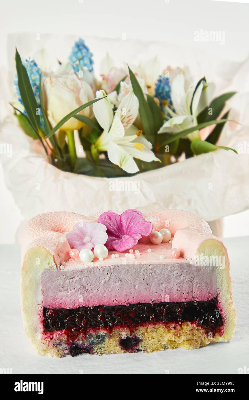 Coupe transversale du gâteau mousse de velours rose avec remplissage de baies et bouquet de fleurs de printemps sur fond blanc. Dessert gastronomique élégant avec espace copie. Banque D'Images