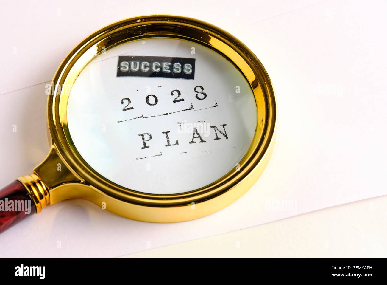La loupe dorée révèle le texte lisant LE PLAN SUCCESS 2028 estampillé sur du papier blanc clair Banque D'Images