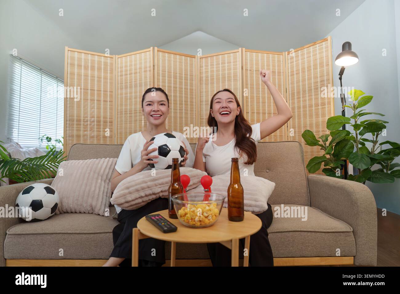 Femmes asiatiques heureuses acclamant tout en regardant un match de football à la maison Banque D'Images