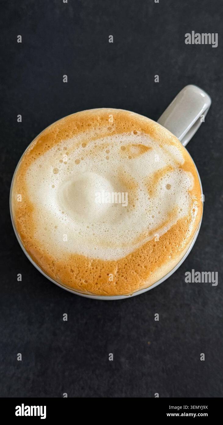 Vue de dessus d'une tasse à café en céramique blanche remplie de cappuccino mousseux sur une surface texturée sombre Banque D'Images