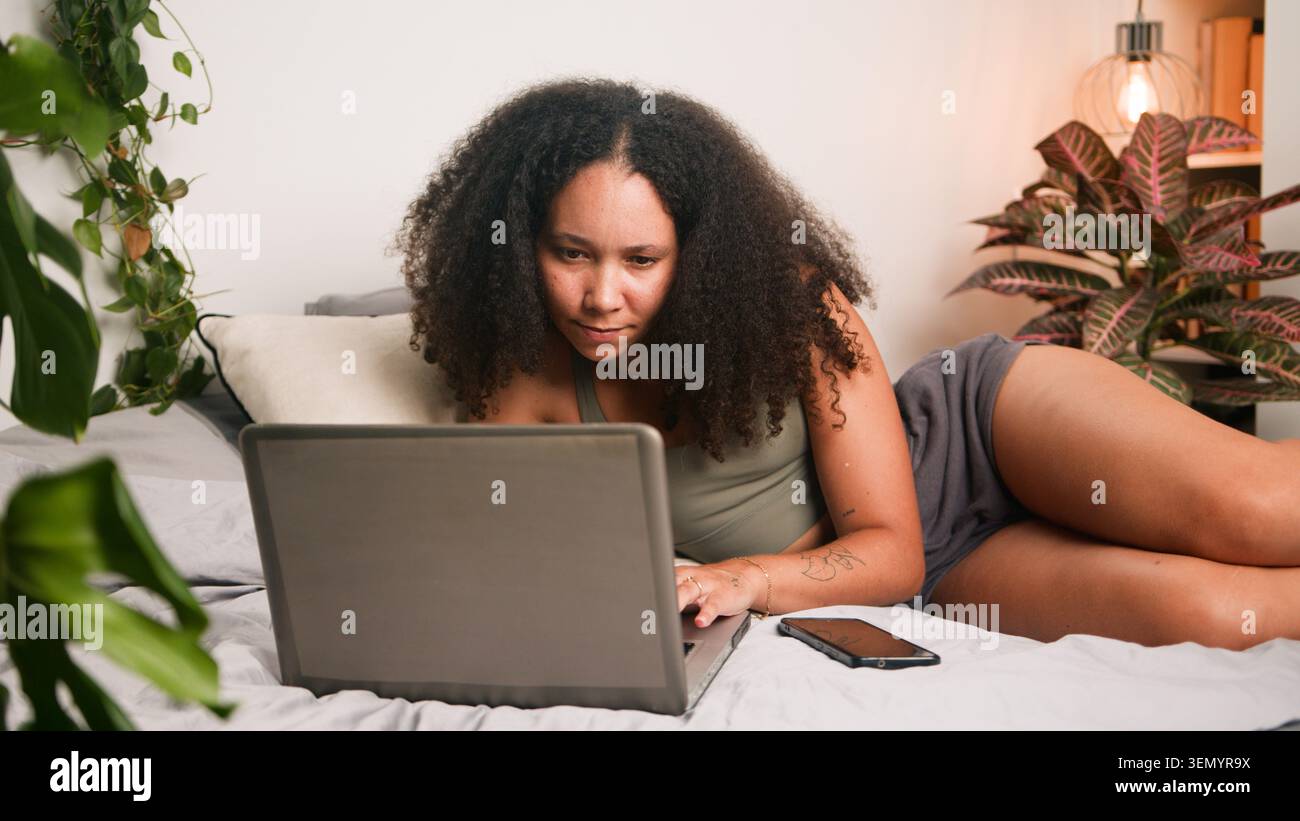 Femme travaillant sur ordinateur portable dans une chambre confortable entourée de plantes et smartphone Banque D'Images