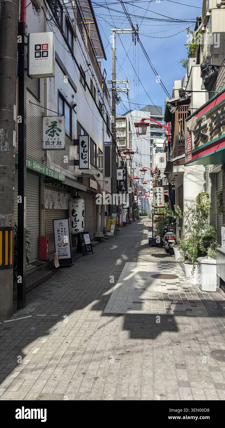 Ruelle commerciale traditionnelle étroite baignée d'une lumière chaude, bordée de boutiques et panneaux japonais à Osaka, Japon Banque D'Images