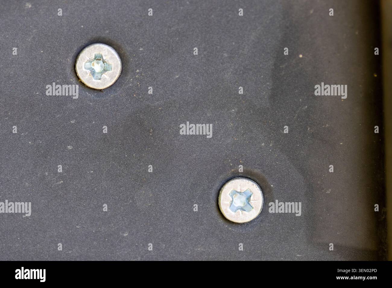 Deux vis Phillips métalliques fixant une plaque métallique texturée foncée, représentant l'assemblage, l'artisanat et les détails de construction Banque D'Images
