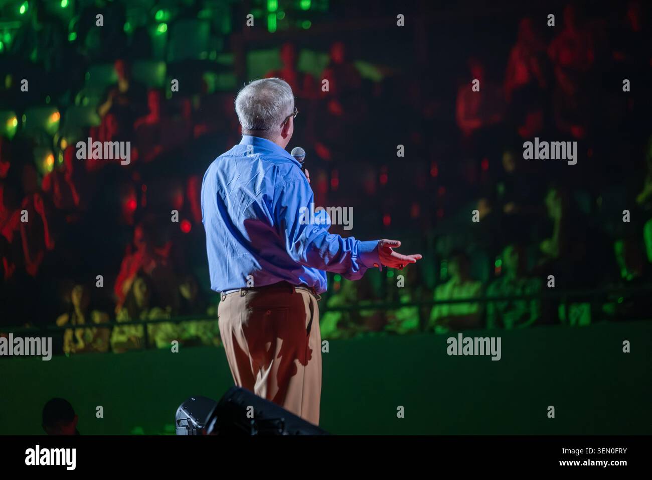 Homme sur scène offrant une présentation au public assis, éclairage vert et rouge spectaculaire, moment de prise de parole en public engagé. Banque D'Images