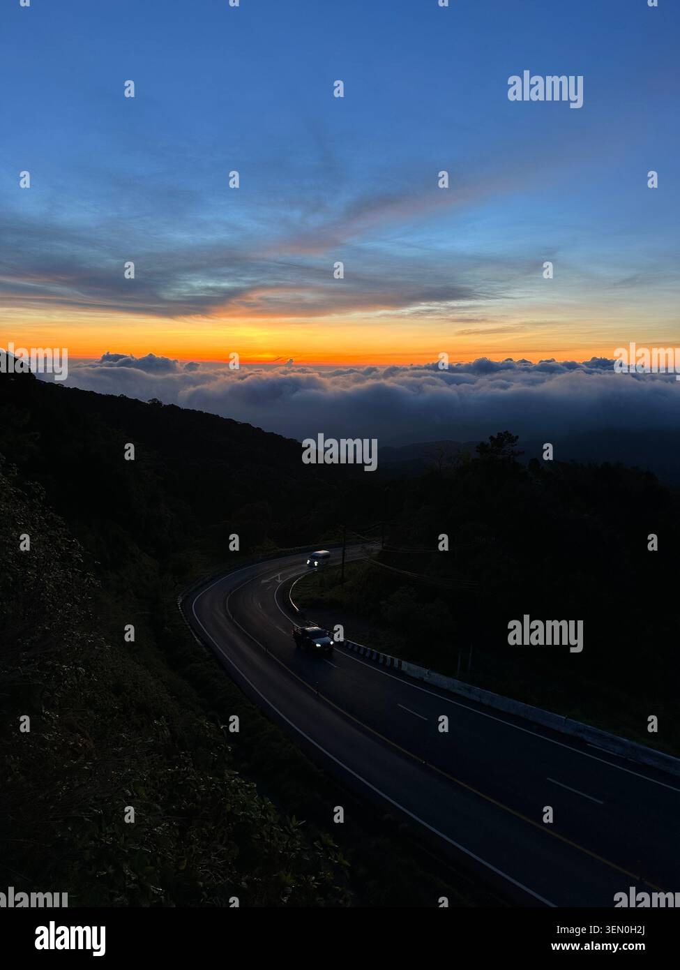 Au-dessus des nuages : une route de montagne sinueuse brille au crépuscule au-dessus d'une mer de nuages près du parc national de Mae Surin, Thaïlande - Image de stock capturée avec un smartphone