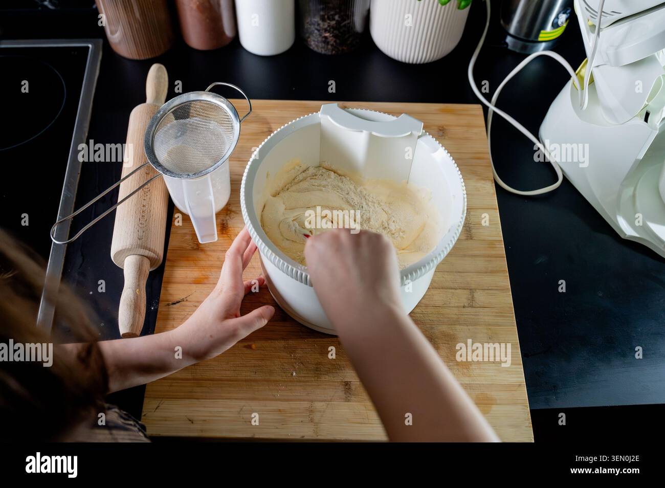 Vue aérienne des mains mélangeant la farine tamisée dans la pâte à gâteau éponge pâle dans un bol sur une planche de bois dans une cuisine moderne, préparant un gâteau fait maison. Banque D'Images