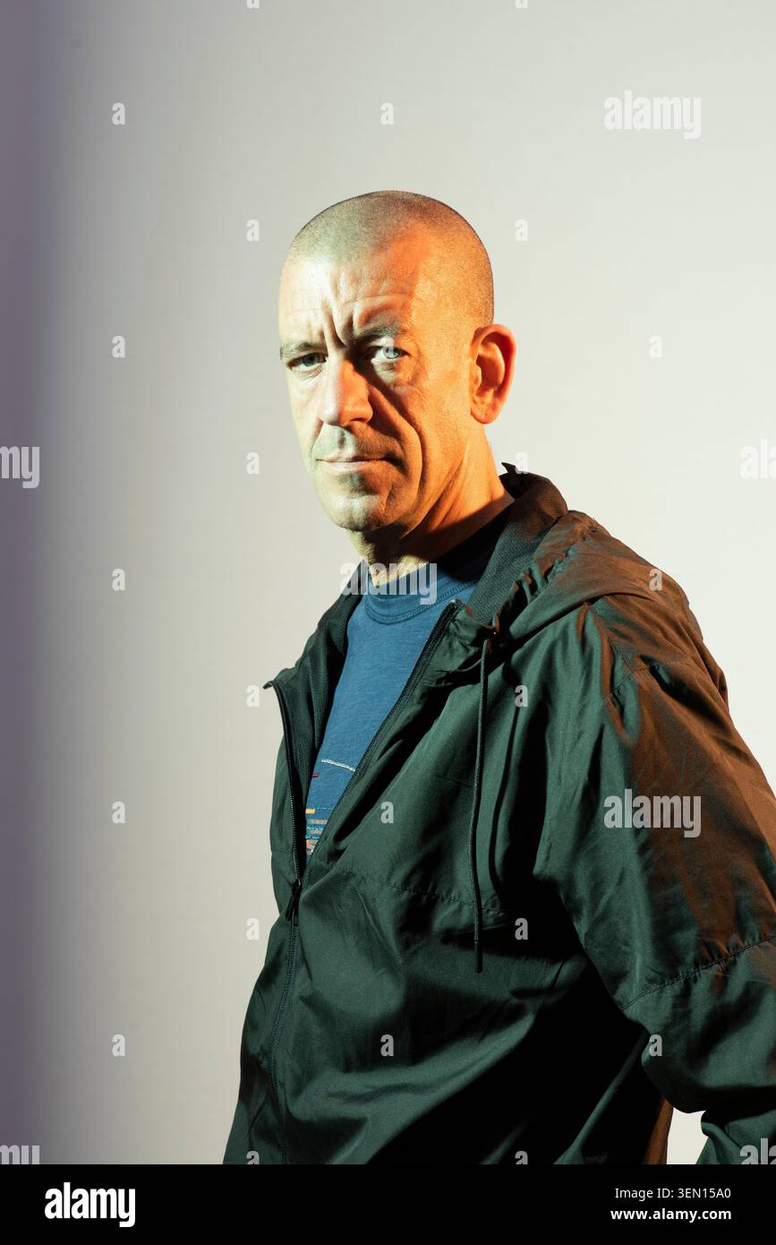 Diarmaid Ferriter se tient face à la caméra dans un studio. Il porte une veste sombre et une chemise bleue. Le fond est vert et orange comme le drapeau irlandais. Banque D'Images