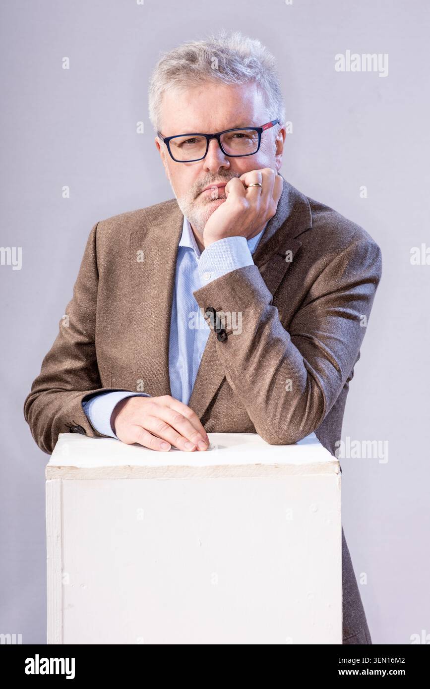 James MacMillan se tient avec une expression sérieuse, reposant son menton sur sa main. Il apparaît profondément dans la pensée, avec un fond neutre et un clair-colo Banque D'Images