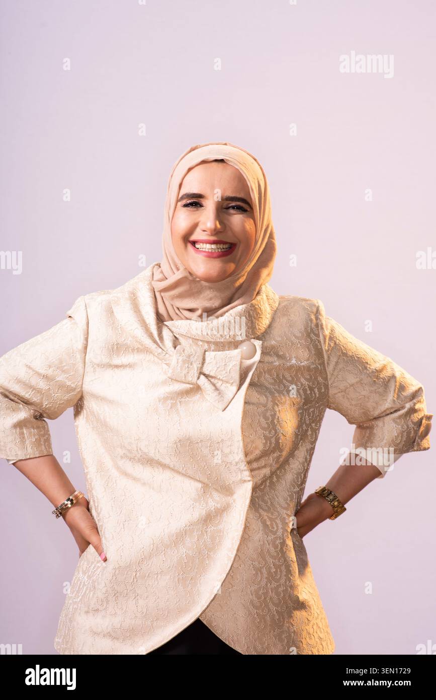 Jokha Alhathri pose avec le sourire tout en portant une tenue de couleur claire et un foulard. L'arrière-plan a une lumière douce et un design simple. Ce SC Banque D'Images