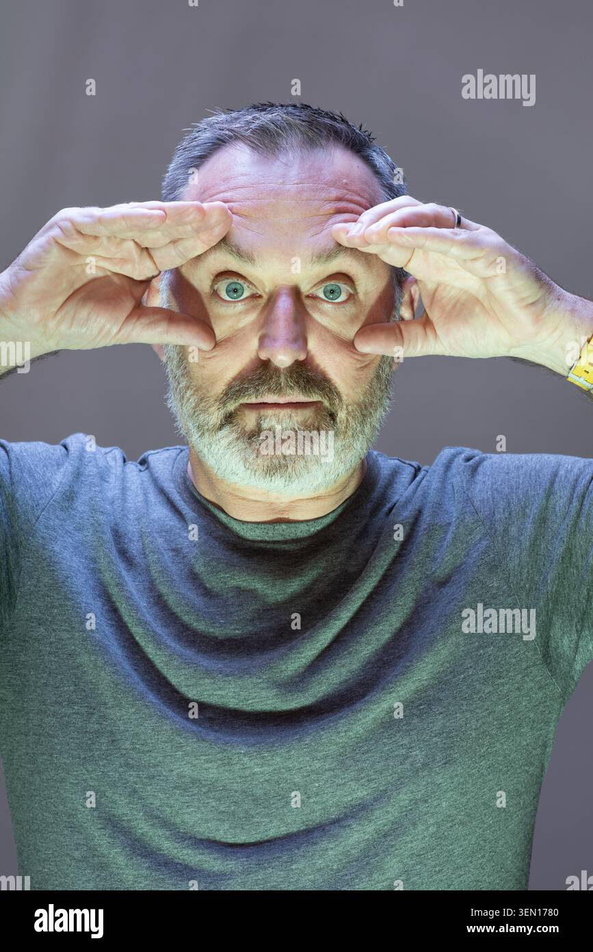Justin Davies fait un visage humoristique dans un cadre de studio. Il utilise ses mains pour tenir ses paupières d'une manière amusante et stupide. L'arrière-plan est simple et Banque D'Images