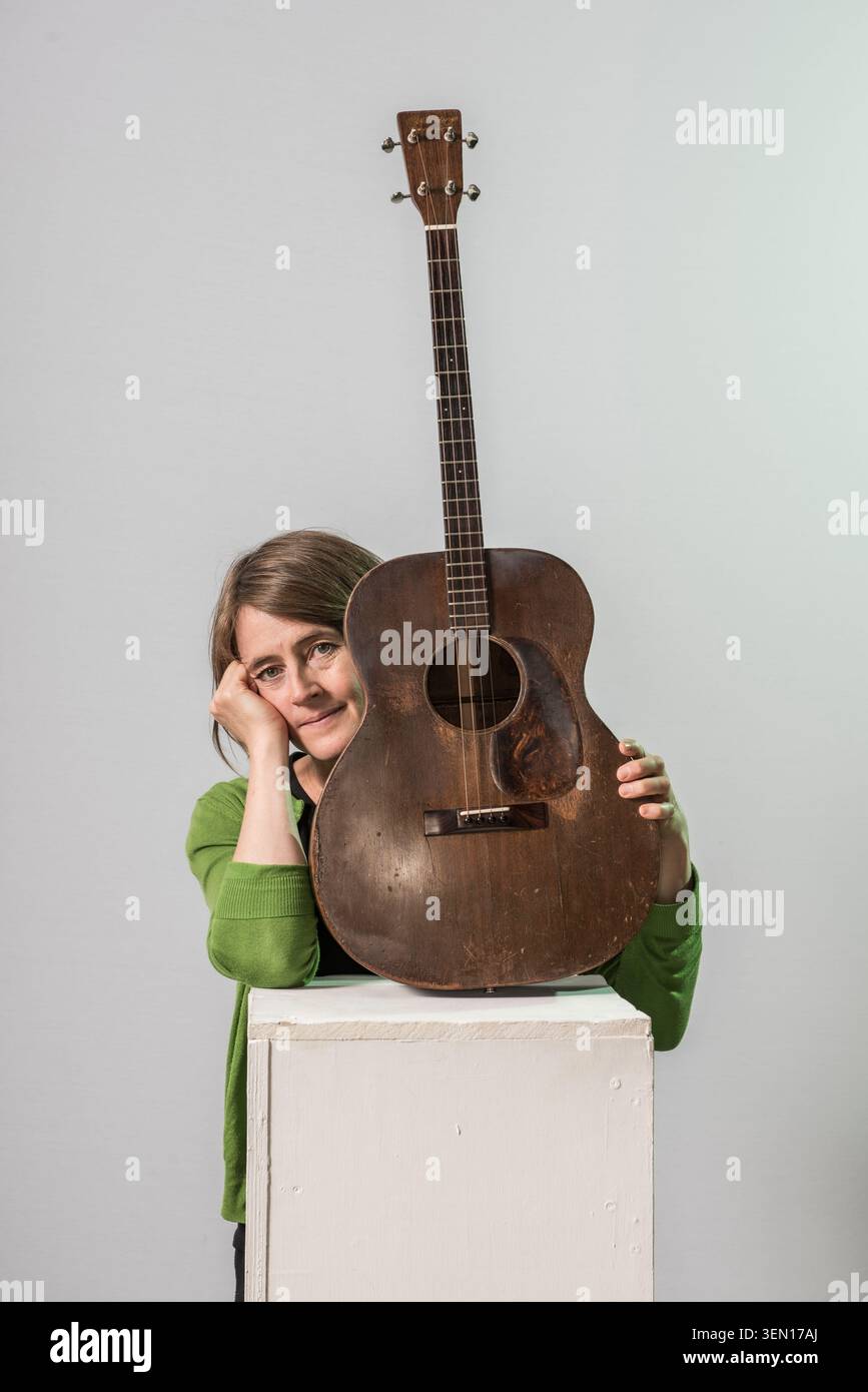 Karine Polwart se tient à côté d'un piédestal blanc, reposant sa tête sur sa main. Elle tient une guitare vintage debout. Le studio a un fond Uni. Th Banque D'Images