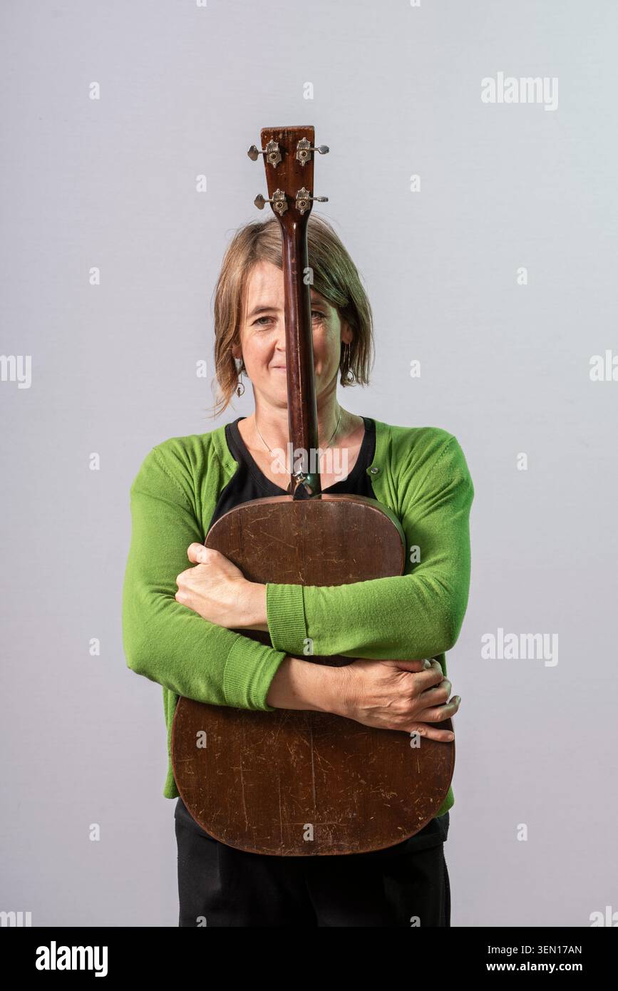 Karine Polwart se tient à l'intérieur, serrant sa guitare. Elle est centrée dans le cadre avec un fond simple. Son expression montre la concentration et le lien avec Banque D'Images