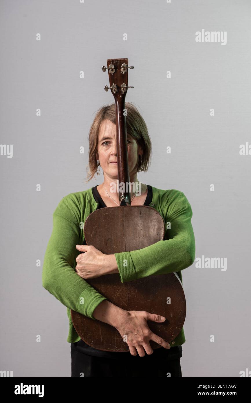 Karine Polwart se tient dans un studio tenant sa guitare près de son corps. Elle regarde directement devant elle avec une expression neutre. Le fond gris contra Banque D'Images