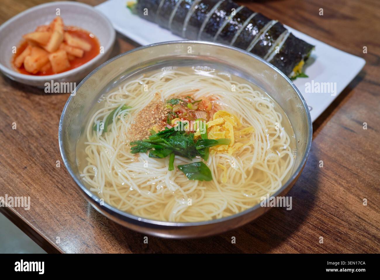 Soupe traditionnelle coréenne chaude aux nouilles, rouleau de riz aux algues tranchées et nouilles épicées mélangées aux légumes frais servies dans d'authentiques bols en acier inoxydable. Banque D'Images