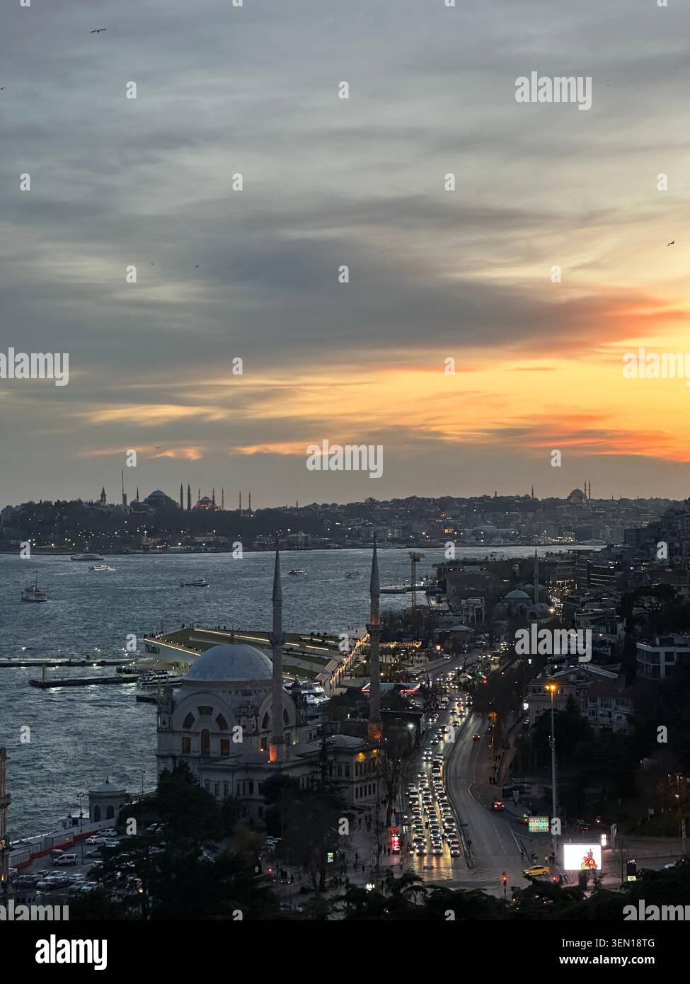 Le coucher de soleil doré adoucit le front de mer d'Istanbul, avec des dômes de mosquées, des lumières de ferry et un rivage animé du Bosphore. - Image de stock capturée avec un smartphone