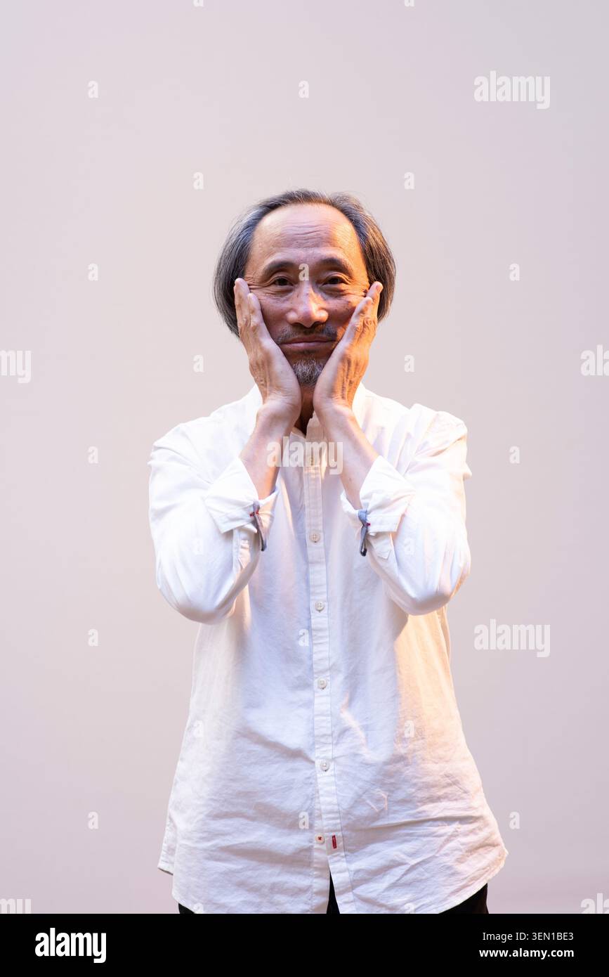 Ma Jian est dans un studio, tenant son visage des deux mains. Il semble exprimer des émotions lors d'une performance. Le réglage est simple, se concentrant sur son A. Banque D'Images