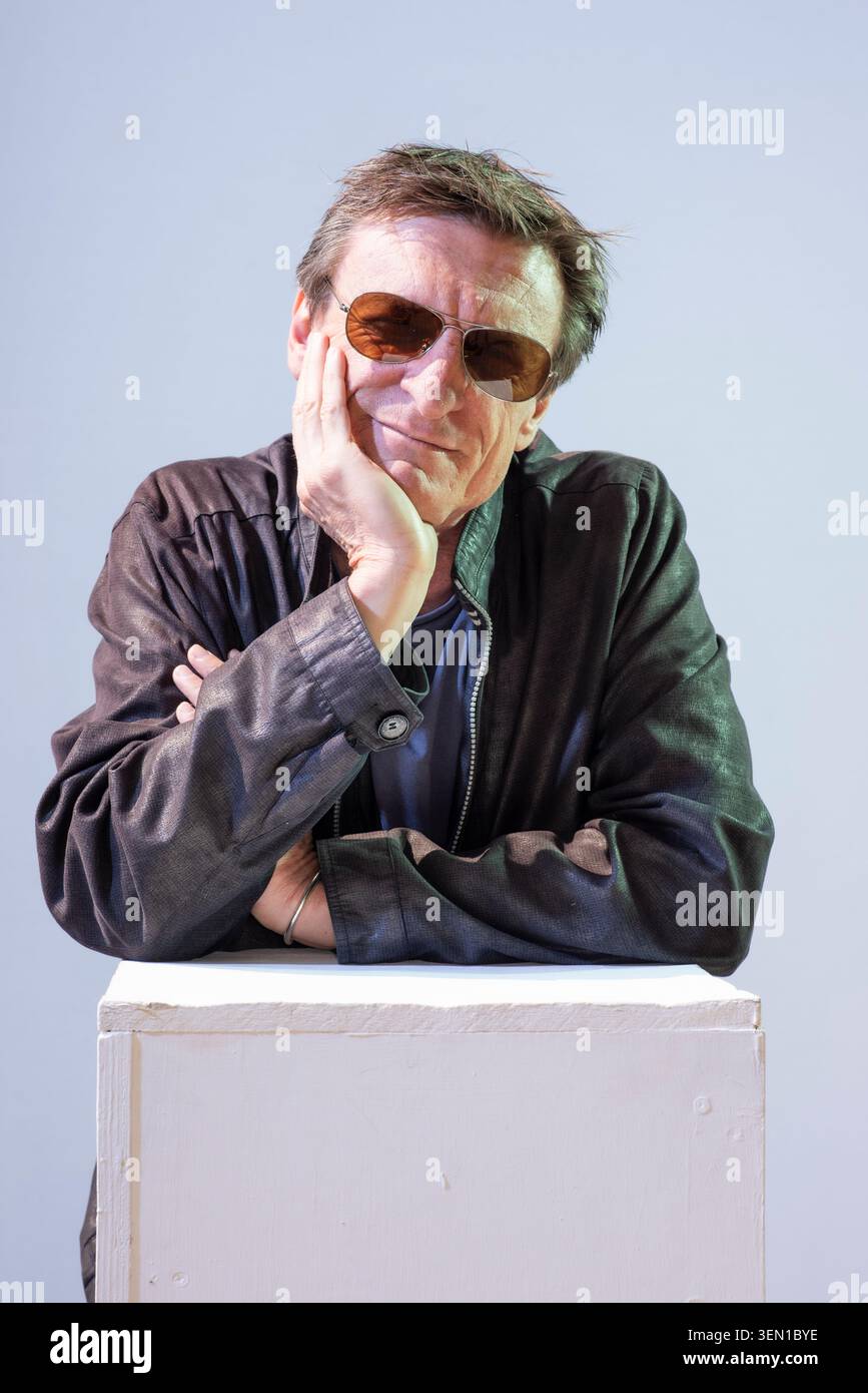 Marcus Malte se tient la main sur le menton, portant des lunettes de soleil, dans un studio. Il s'appuie contre un piédestal blanc. Le regard suggère qu'il réfléchit Banque D'Images