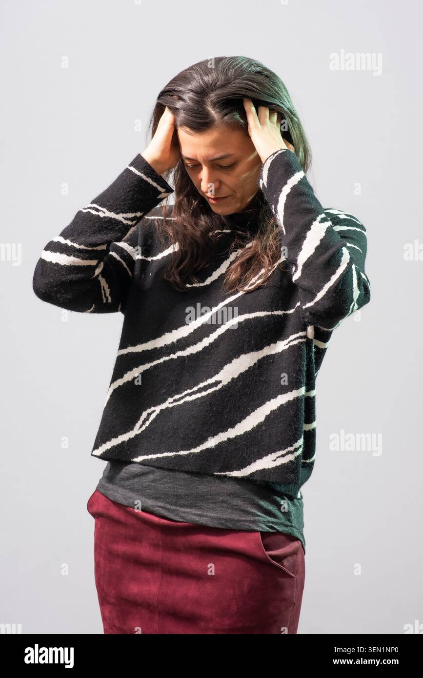 Samanta Schweblin se tient dans un studio tenant sa tête des deux mains. Elle porte un pull rayé noir et blanc. Le fond est simple avec neut Banque D'Images