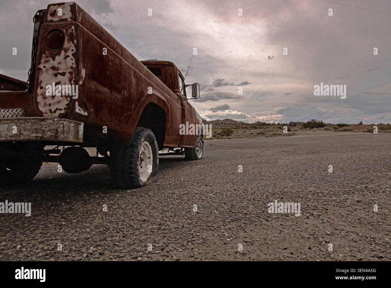 Camion vintage rouillé abandonné avec un pneu crevé sur une route désertique de gravier sous un ciel nuageux Banque D'Images