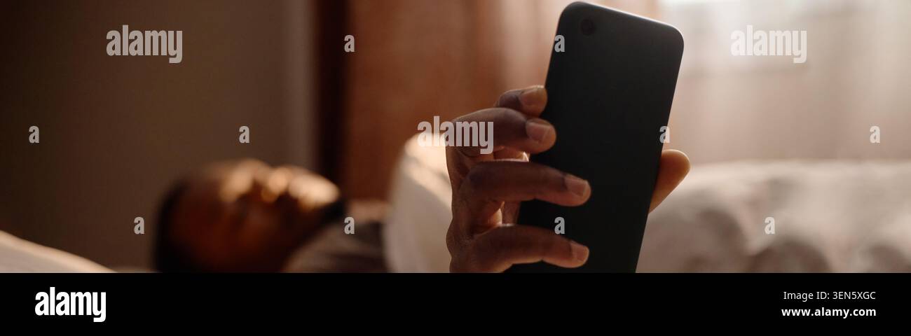Homme noir utilisant smartphone dans le lit pour le concept de dépendance numérique Banque D'Images