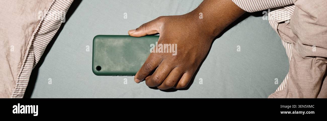 Adulte tenant le smartphone dans le lit montrant la fatigue numérique Banque D'Images