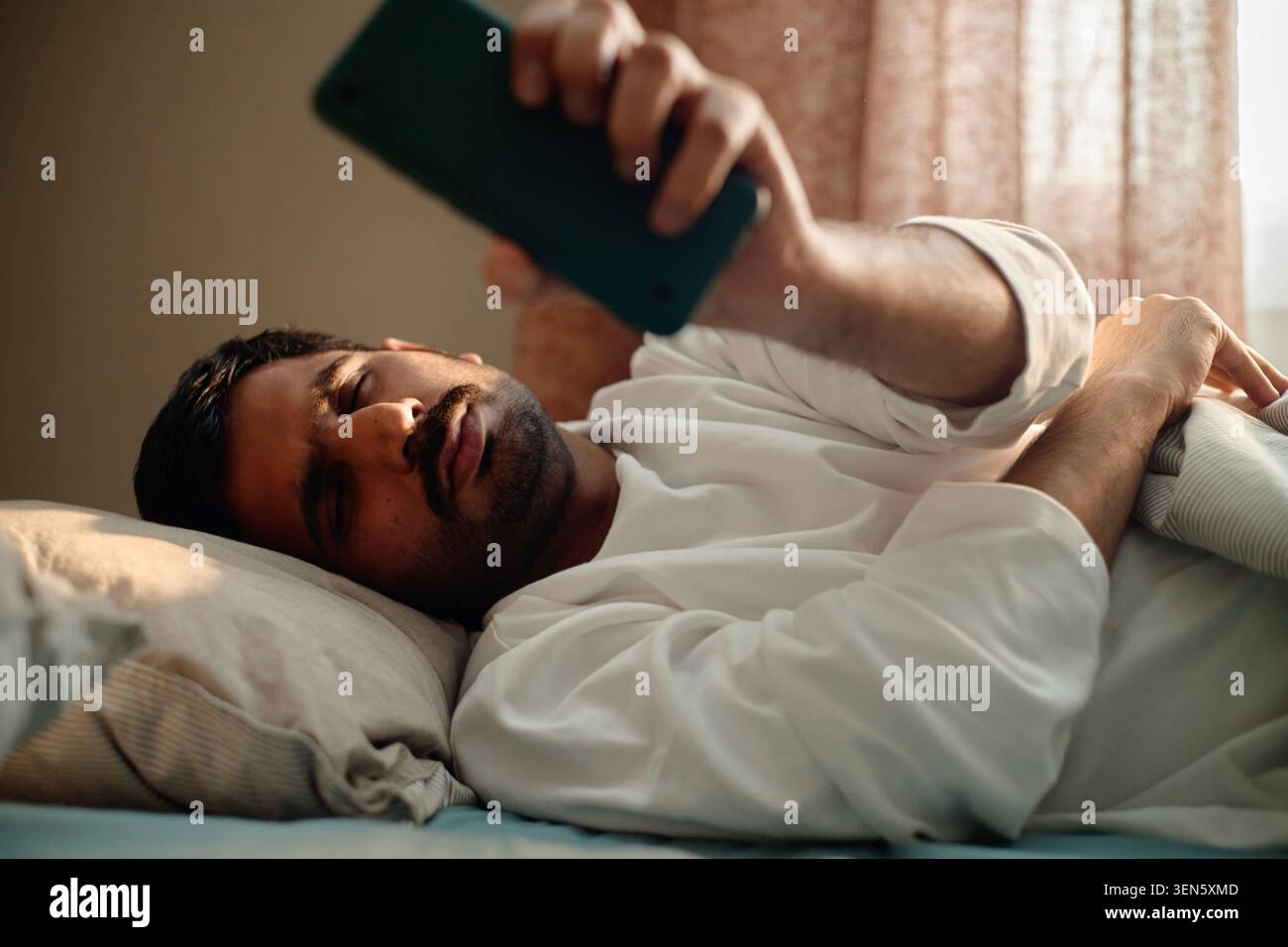 Homme adulte atteignant pour smartphone dans le lit pour l'habitude de temps d'écran Banque D'Images