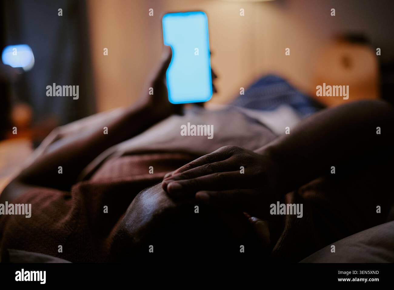 Homme noir couché dans le lit tenant smartphone pour perturbation du sommeil Banque D'Images