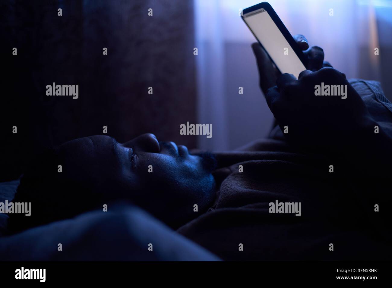 Homme noir utilisant un smartphone dans le lit montrant la dépendance numérique Banque D'Images