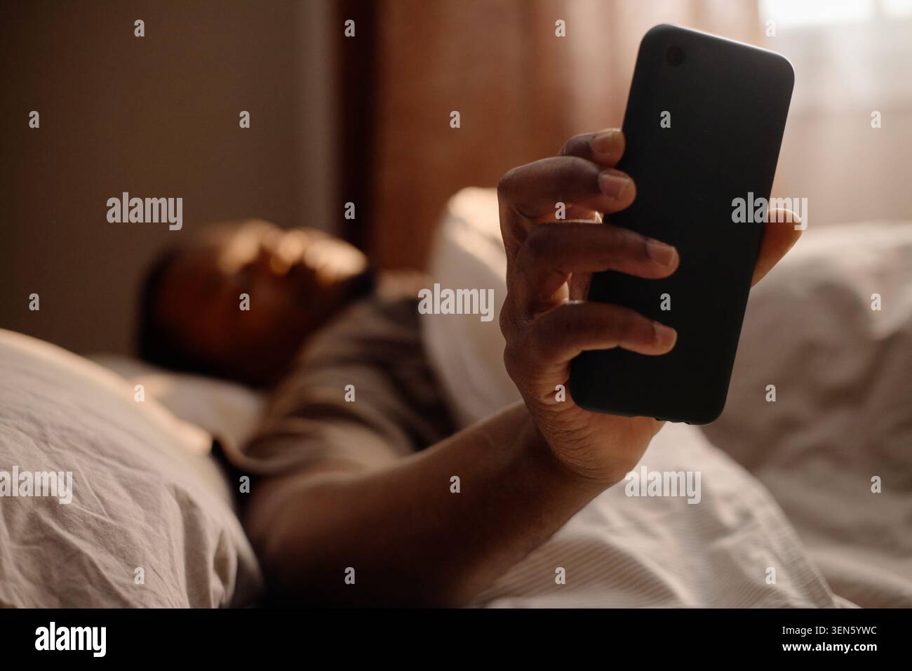 Homme noir tenant smartphone dans le lit pour la dépendance de l'écran de nuit tardive Banque D'Images